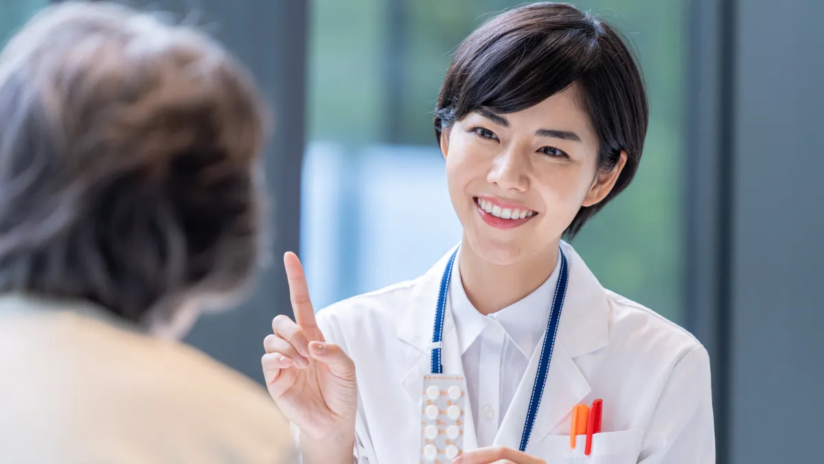 白衣を着た女性が錠剤を持って女性に話している