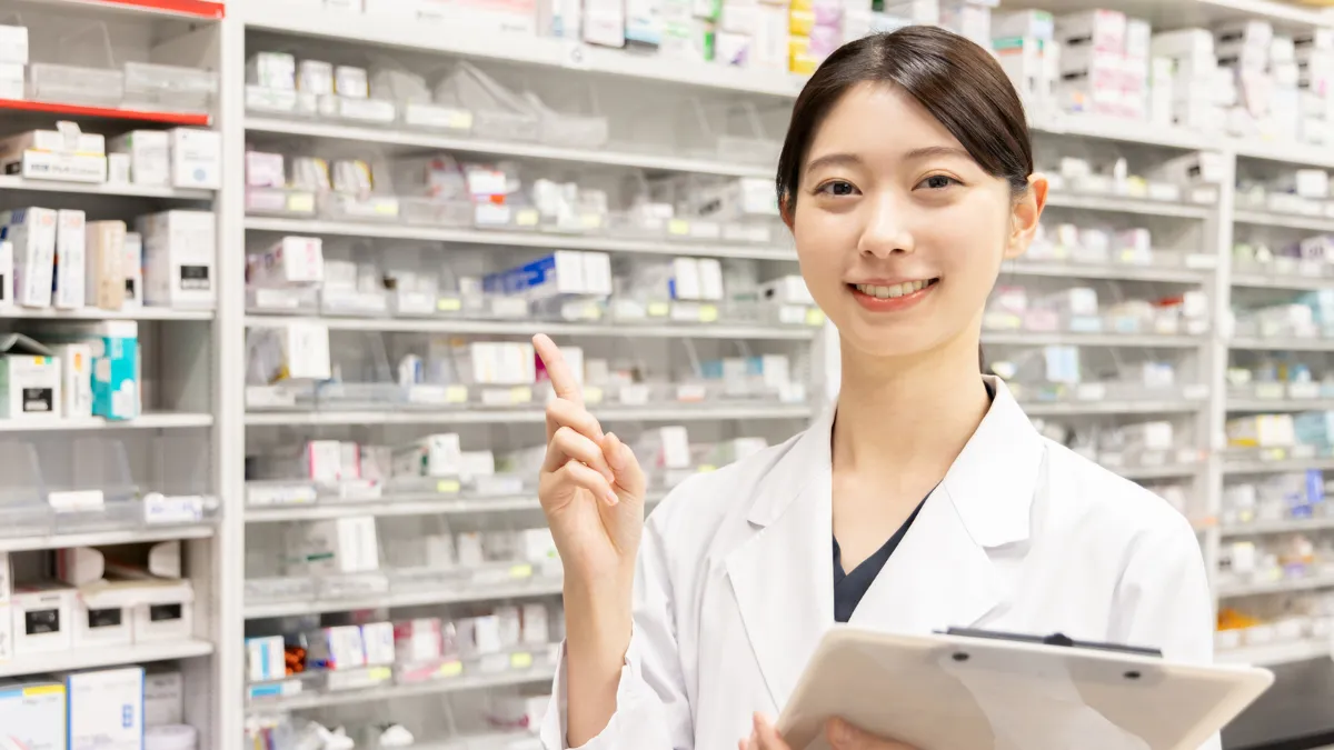 薬ケースの前で白衣を着た女性が笑顔で立ってる