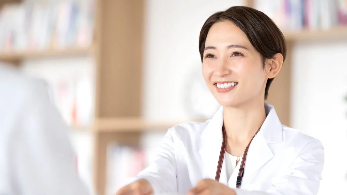 白衣を着た女性が笑顔で薬袋を持ちながら話している