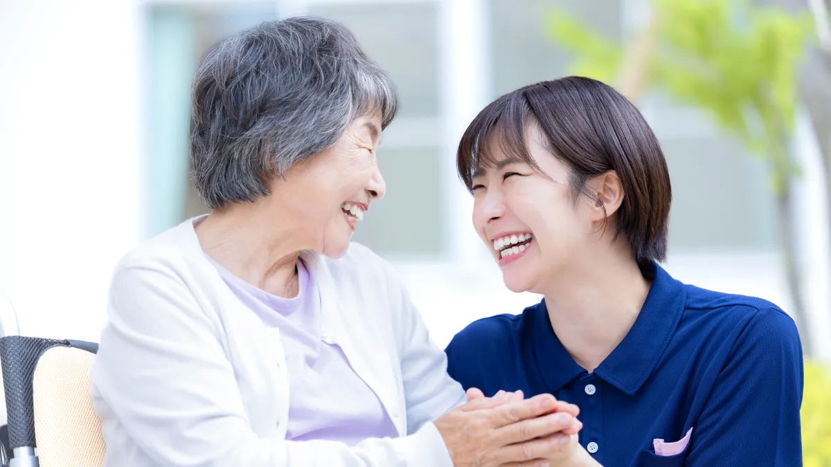スクラブを着た女性が車いすの女性と手を握って笑顔で話している