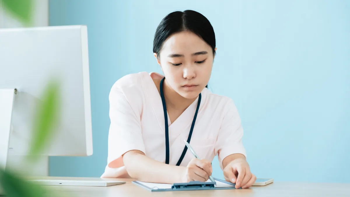 白衣を着た女性がパソコンの前に座ってバンに何か書き込んでいる