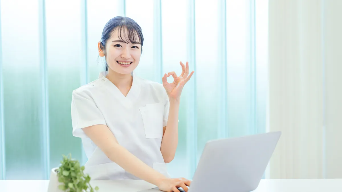 白衣の女性がパソコンを開いて座っている