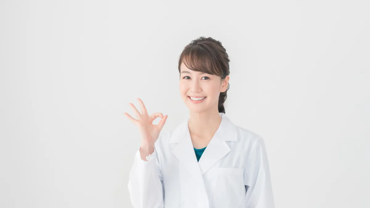 白衣を着た女性が笑顔で丸サインをしている