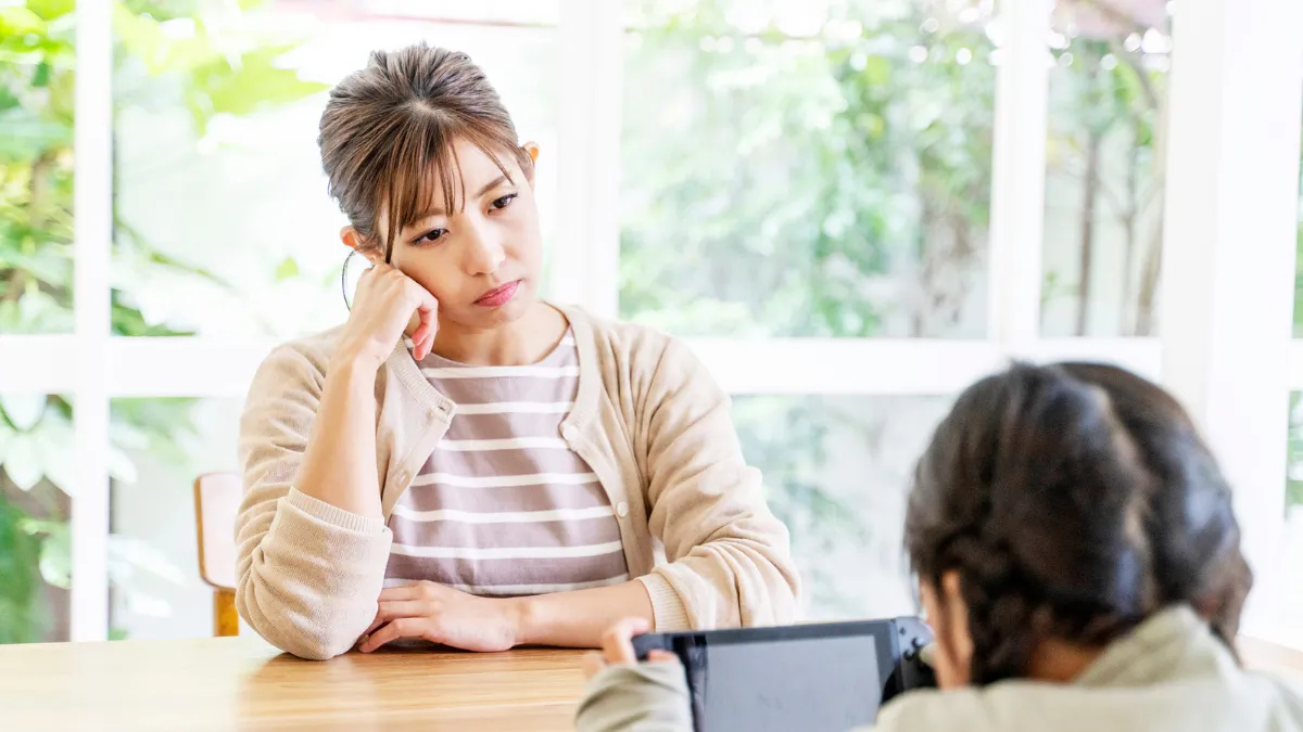 険しい表情の女性の前でゲームをしている子供