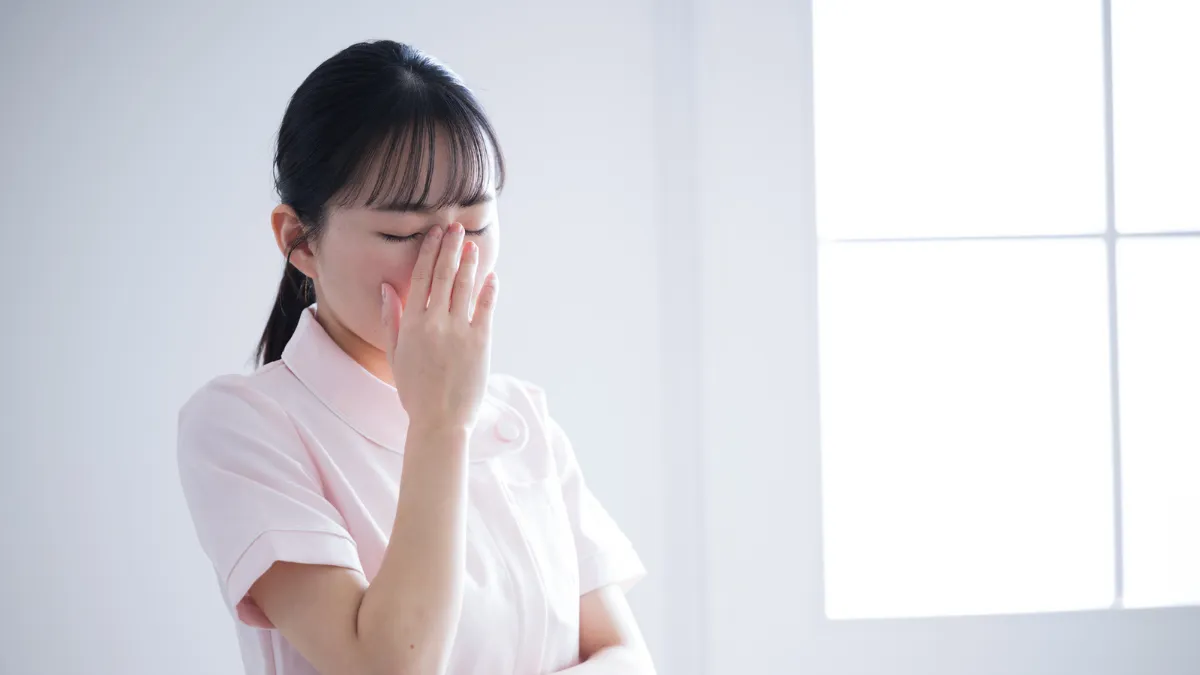白衣を着た女性が額に手を当てて悩んでいる