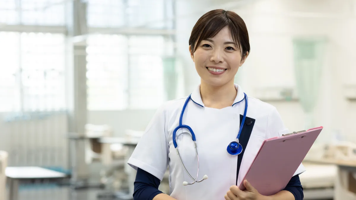 病室で聴診器とバインダーを持って笑顔の看護師