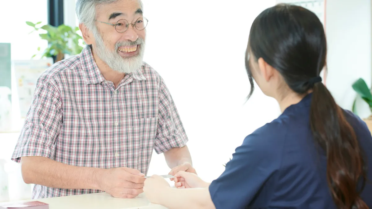 鍼灸院の受付で男性患者さんに笑顔で対応する鍼灸師