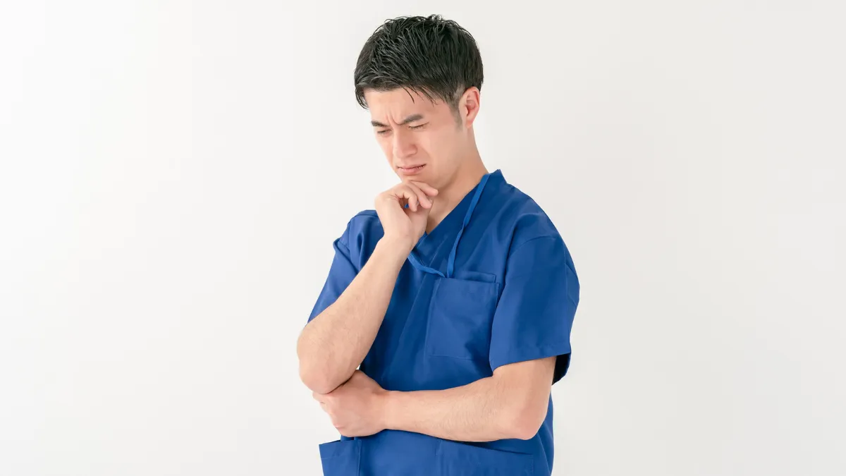 腕を組み顎に手をあてて悩む男性鍼灸師
