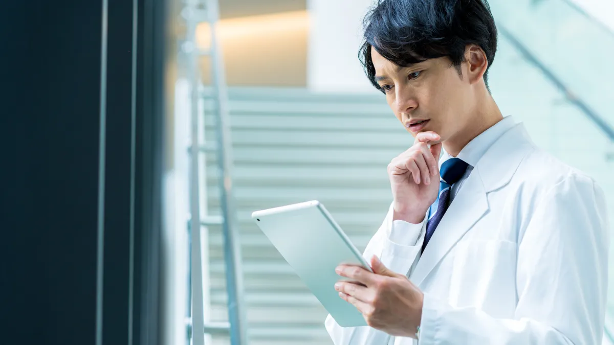 薬剤師の男性がタブレットを眺めながら悩んでいる