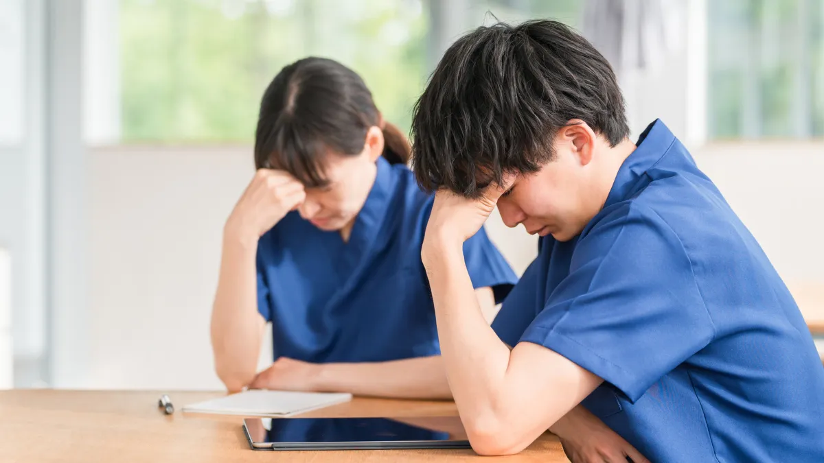 柔道整復師の男女スタッフがタブレットを前に頭を抱えて悩んでいる様子