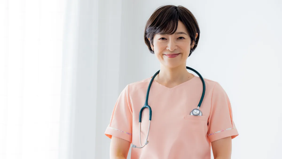 窓際に立つベテラン看護師が聴診器を持っている様子