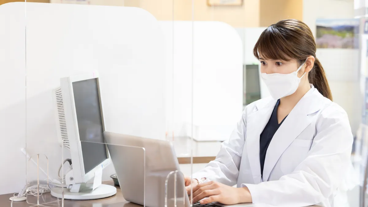 マスクを着けてパソコンで研究データを扱う女性薬剤師