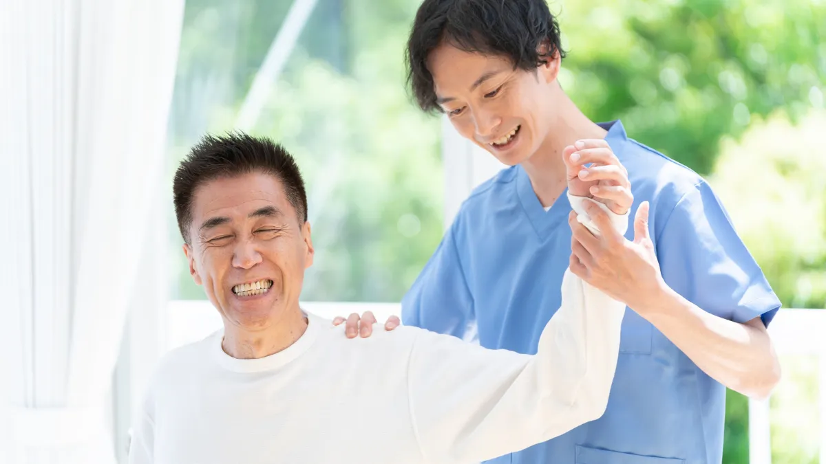 高齢の男性利用者さんの肩を和やかに施術するあん摩マッサージ指圧師