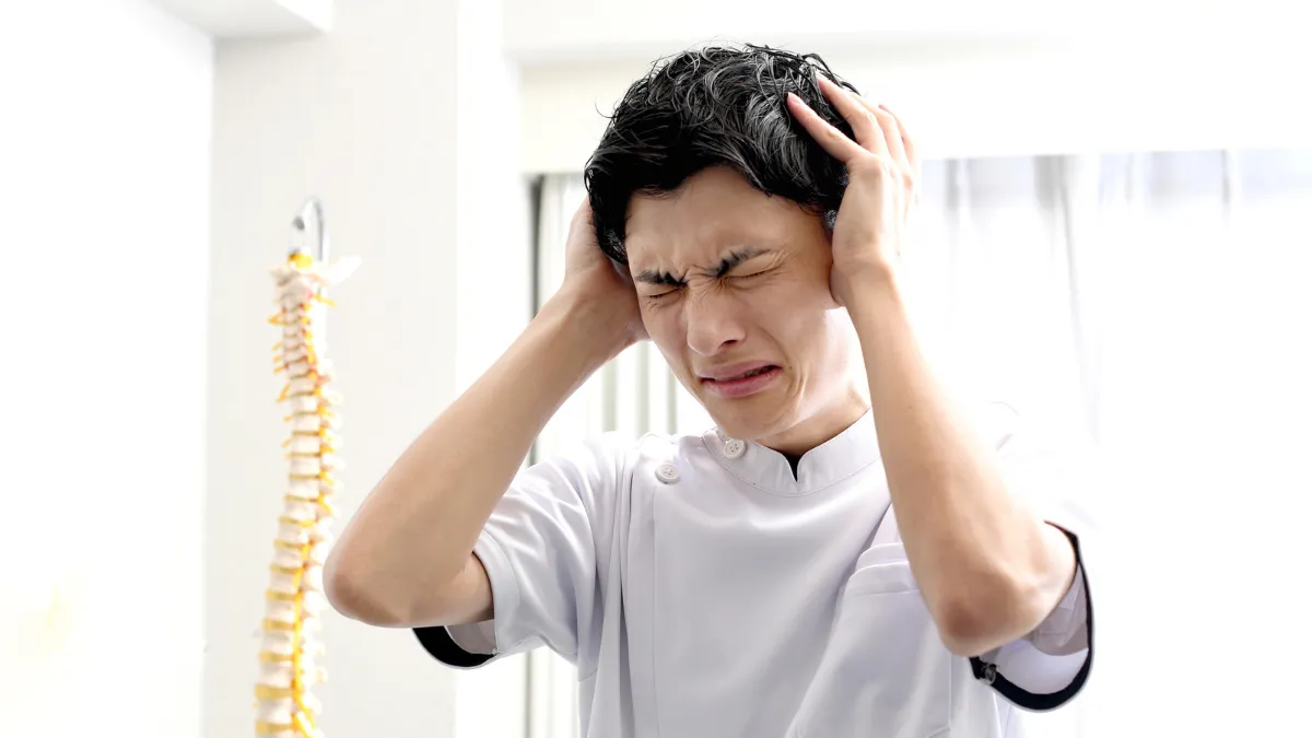 人骨模型の前で頭を抱える鍼灸師の男性