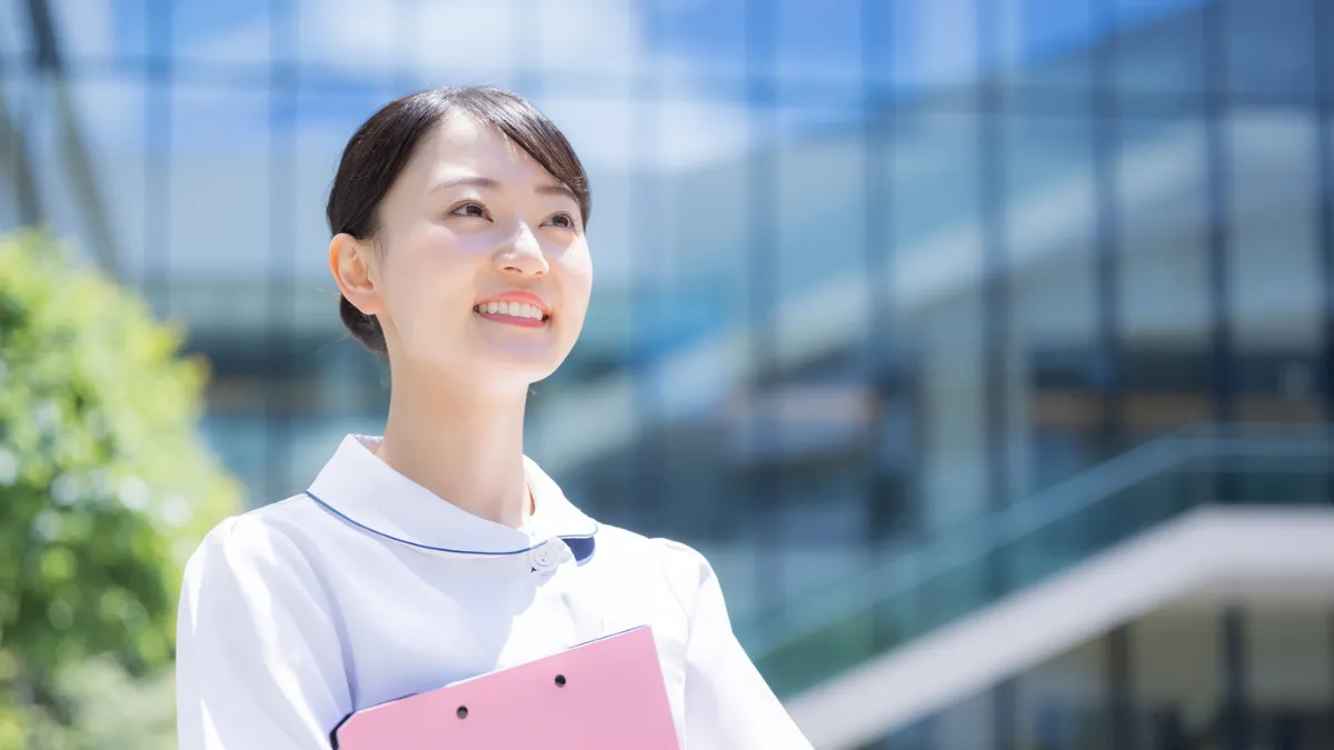屋外でバインダーを持ち前を見つめる看護師