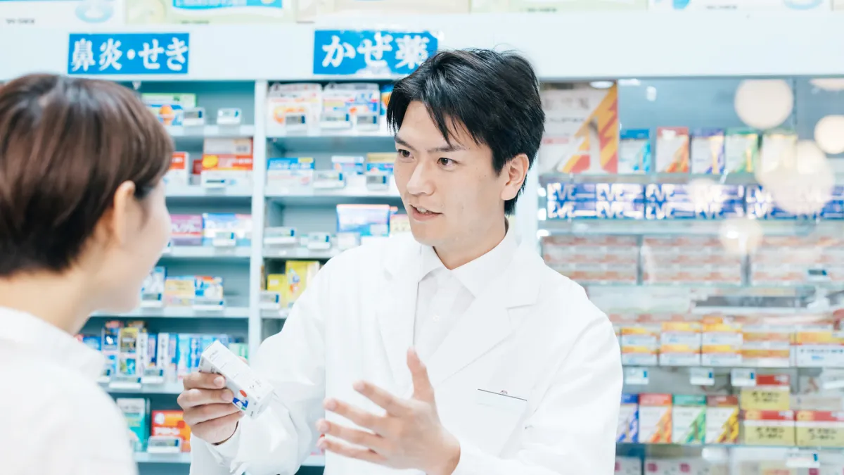 ドラッグストアで来店者に薬を説明する薬剤師