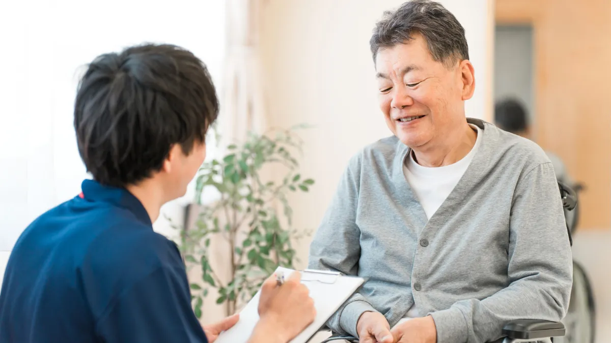 車いすの高齢の利用者さんに問診する鍼灸師