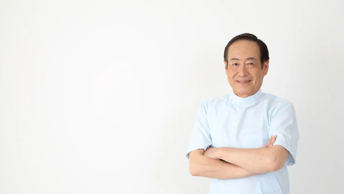 腕を組んで立つベテランの年配男性鍼灸師