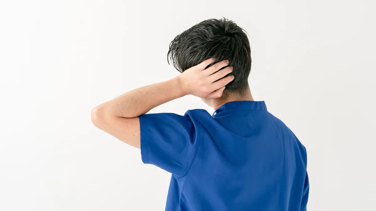 後頭部に手を置いて悩む様子の男性鍼灸師
