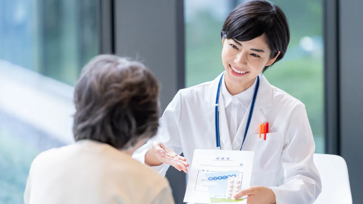 お薬手帳を手に笑顔で説明する薬剤師
